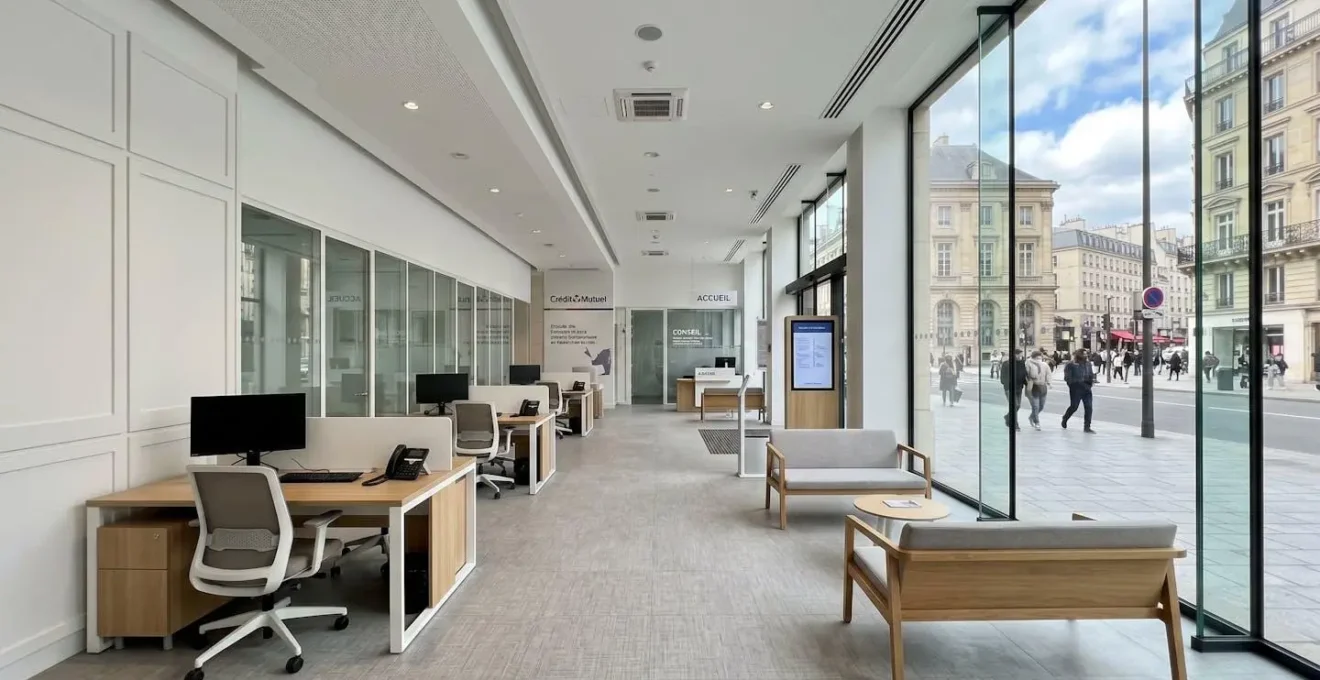Intérieur d'une agence bancaire moderne avec de grandes baies vitrées laissant entrer la lumière naturelle et du mobilier contemporain